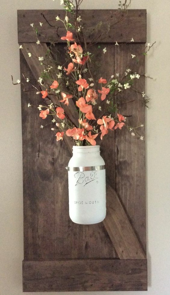 vase blanche avec fleurs oranges accrochés à un panneau en planches de bois