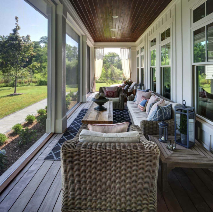 aménagement veranda, chaises en rotin, coussins géométriques, table basse en bois, fenêtres blanches 