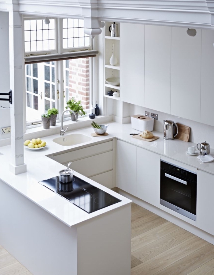 cuisine total blanc au plancher bois avec fenêtre et four noir, exemple de cuisine en u avec bar, idée rangement vertical ouvert