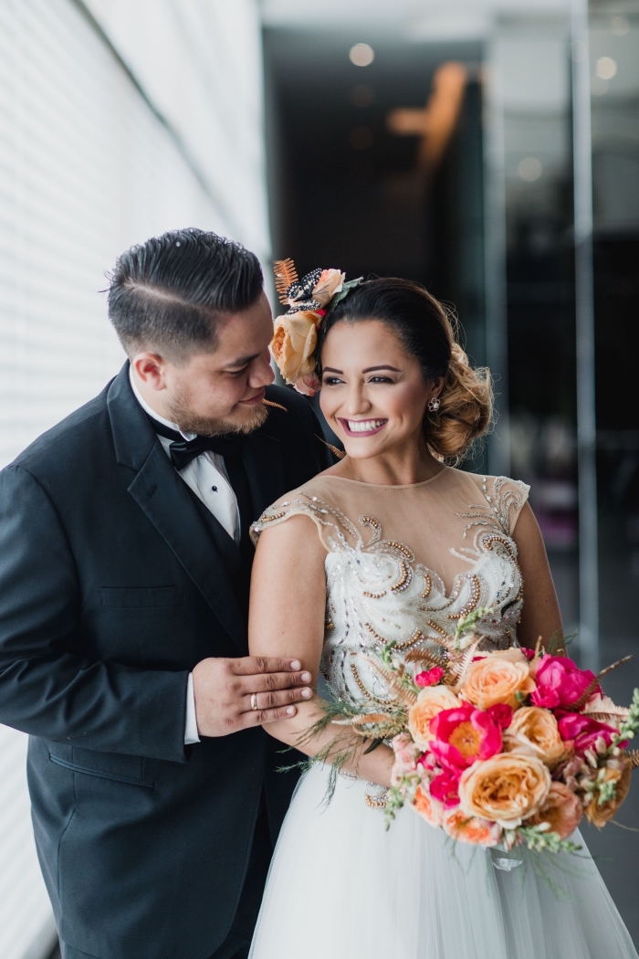 chignon de mariage bouclé sur le côté avec accessoire fleuri, idée coiffure pour robe avec décolleté transparent