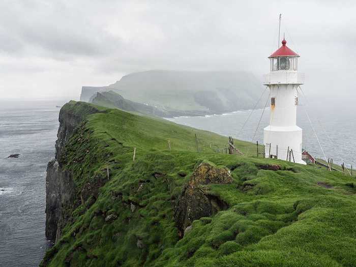 Les iles Faroe, islande paysage, la beauté de la terre, les plus beaux paysages du monde, phare sur un colin vert entouré de l'océan et un grand lac