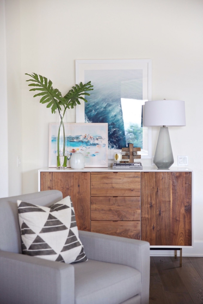 exemple de décoration style bord de mer avec photos océaniques, pièce beige aménagée avec meubles bois foncé et canapé gris