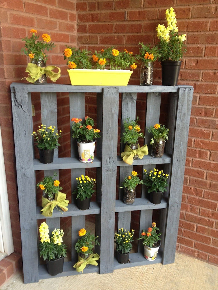 palette de bois recyclée et repeinte en gris, avec des étagères de rangement à plusieurs pots de fleurs
