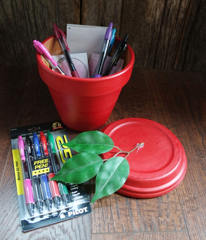 cadeau merci maitresse, idee de pot de fleur repeint en rouge avec motif pomme et branche de feuilles vertes en top, stylos à l intérieur d un pot