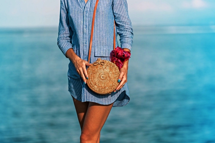 tunique de plage chic à fines rayures accessoirisée avec un sac bandoulière rond tressé, robe chemise boutonnée devant pour aller à la plage