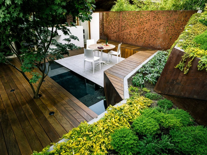 aménagement extérieur originale, terrasses en bois, parterres de plantes vertes, piscine enterrée et terrasse avec petite table