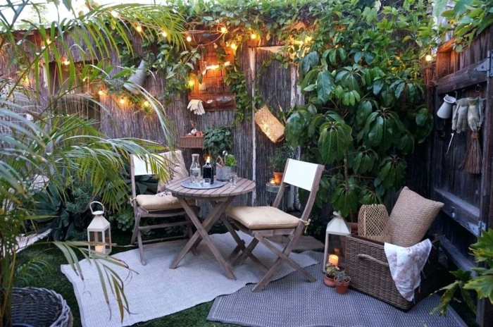 jardin paysager, table et chaises, panier rustique, coussin en jute, lanternes grecques, guirlande lumineuse, salon de jardin coquet