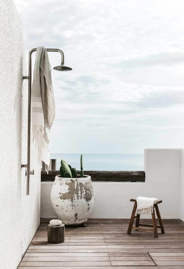 design minimaliste dans une salle de bain extérieure sur terrasse aux murs blancs et sol en planches de bois avec douche métal