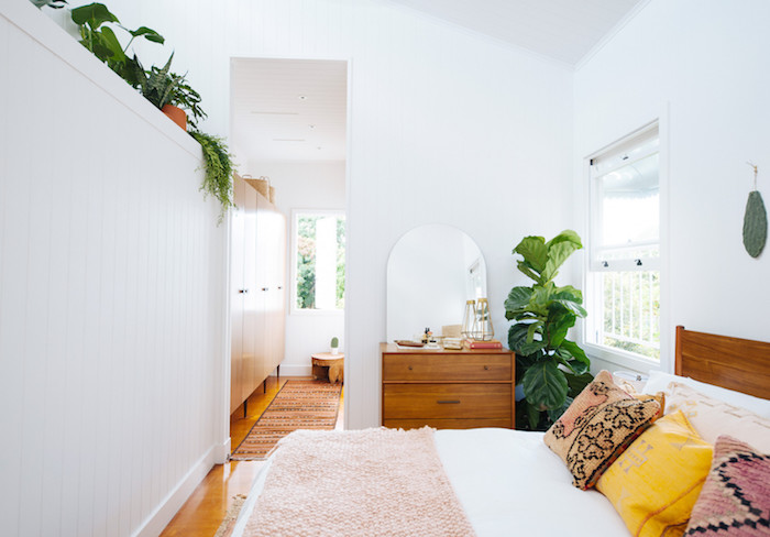 deco chambre boheme chic avec lit bois à linge blanc et plaid rose, coussins colorés, commode bois, murs blancs, plante verte en pot et végétation en hauteur