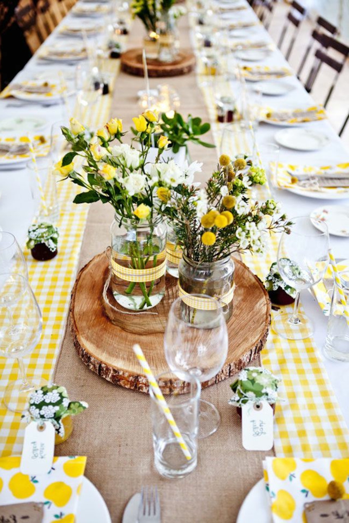 chemin de table carreaux jaunes et blancs, rondins de bois, vases en verre, bouquets de fleurs des champs