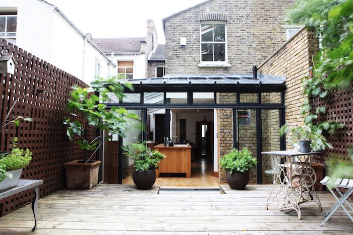extension pour abriter une cuisine avec ilot central bois ouverte sur terrasse de bois avec végétaux et petit salon de jardin