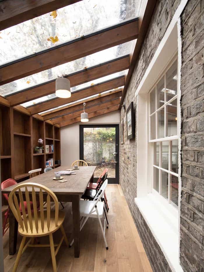 extension ossature bois et vitres pour abriter une salle à manger avec table à diner bois et chaises dépareillées sur parquet bois, mur de rangement