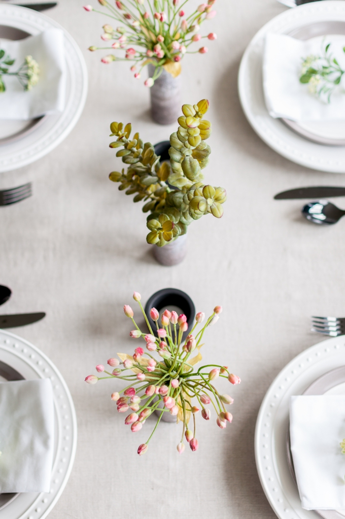 centre de table avec vases cylindriques au aspect béton, assiettes blanches, ustensiles sur la table de fête