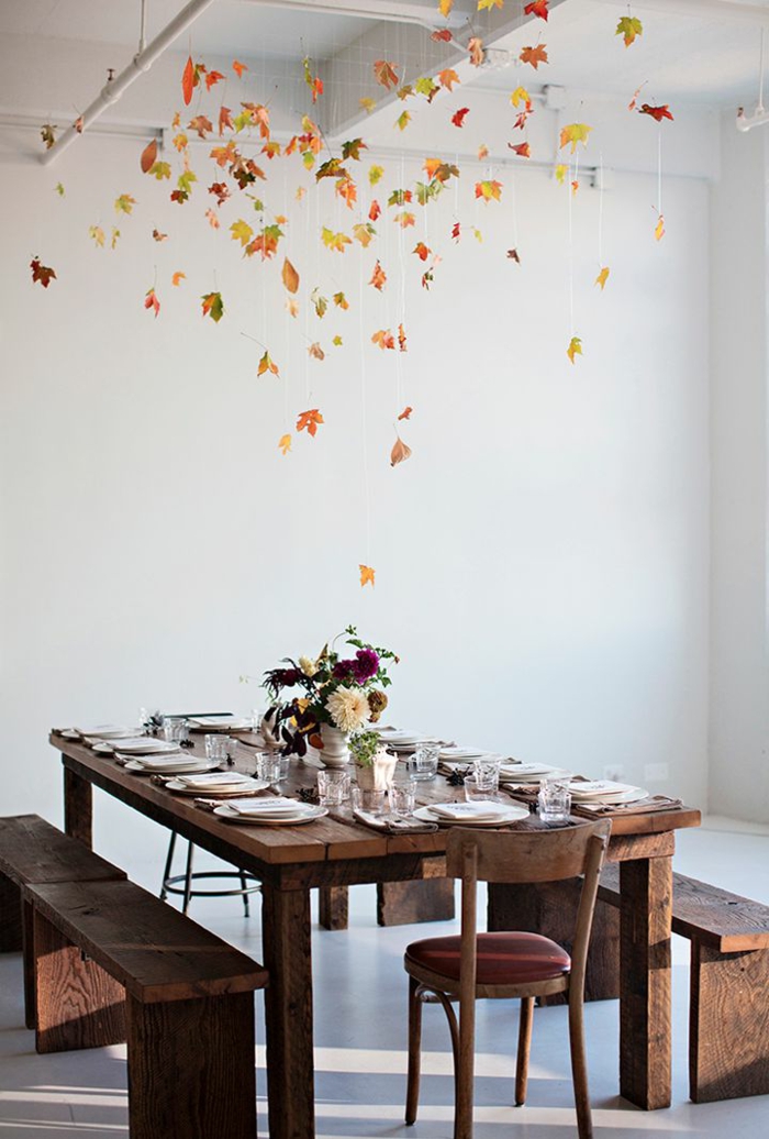 table de repas décorée, assiettes blanches sur table en bois foncé, centre de table vase, guirlande en feuilles d'automne