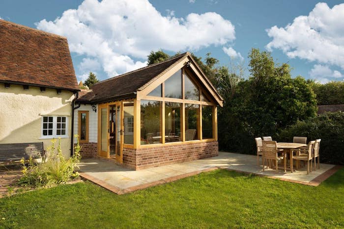 extension bois sur une terrasse en carrelage beige avec une petite salle à manger en plein air à coté, gazon vert