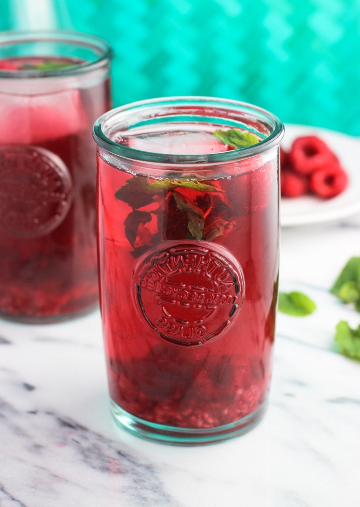 recette de thé vert refroidi servi avec feuilles de menthes et framboises, idée ice tea maison rouge aux framboises