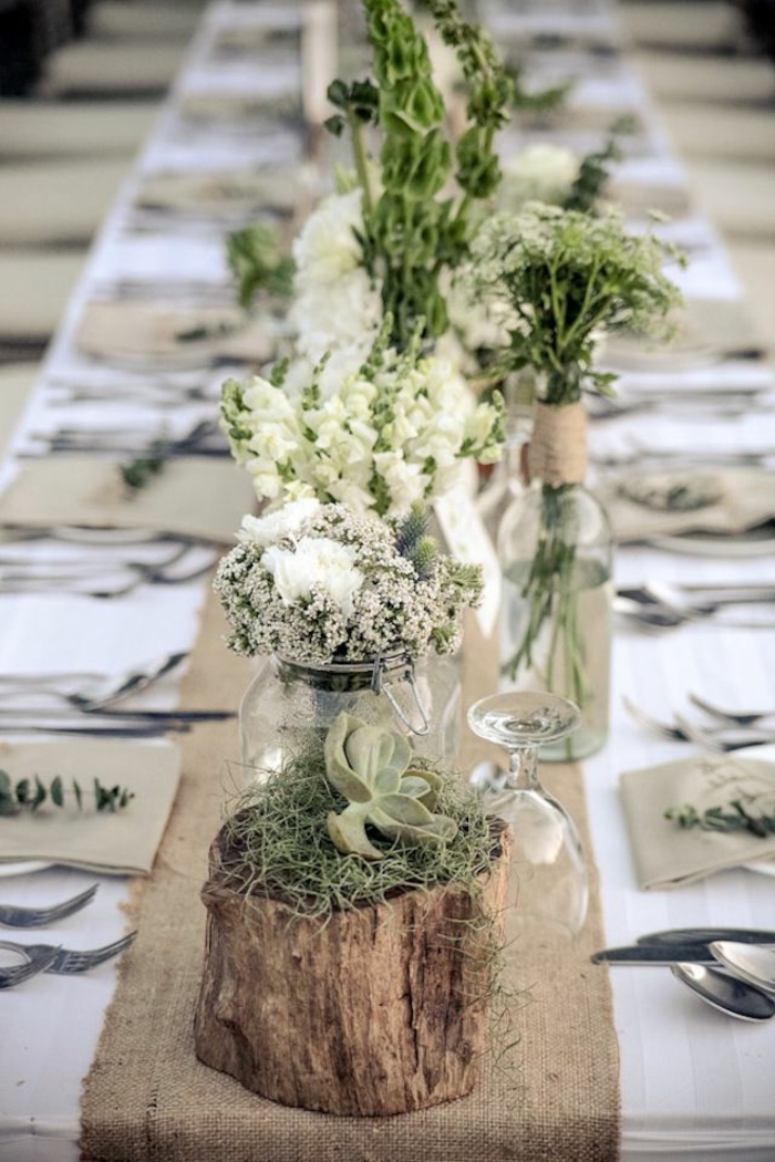 tronc de bois avec vases, petits arrangement blancs, nappes de table blanches, mousse verte