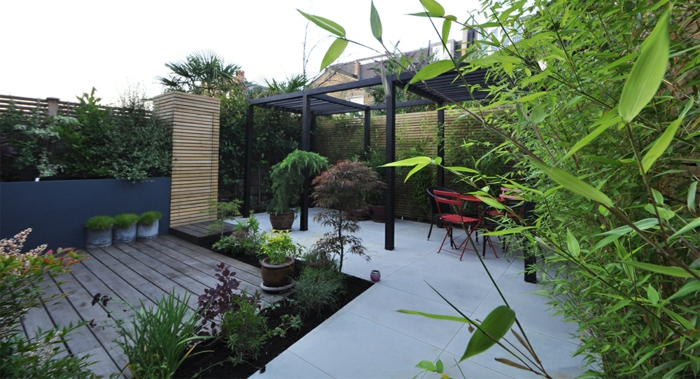 grande terrasse en béton, tonnelle noire, terrasse en bois, bambous plantés, pots de fleur, amenagement jardin paysager