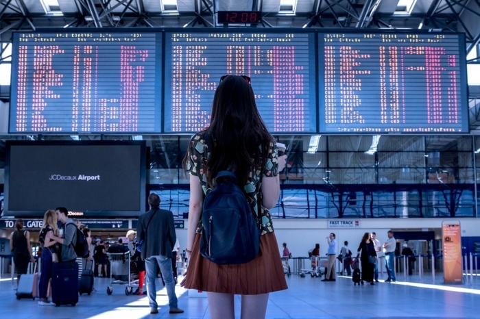 jeune fille devant le tableau d aéroport, grande salle d attente, aéroport, sac à dos, jupe couleur terracotta