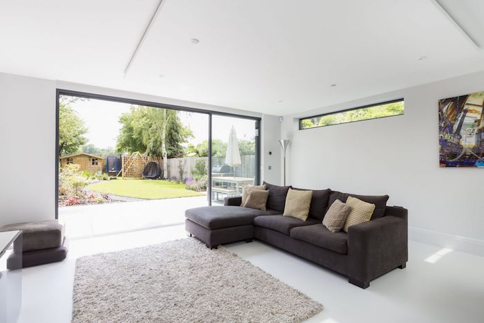 murs blancs et style minimaliste d amengemeent extension garage avec tapis gris clair et canapé gris foncé