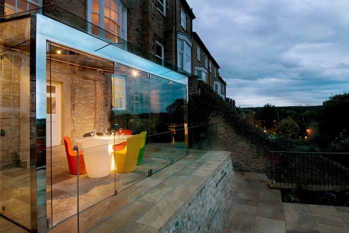 extension vitrée avec une table à éclairage LED entourée de fauteuils dépareillées sur terrasse exterieure