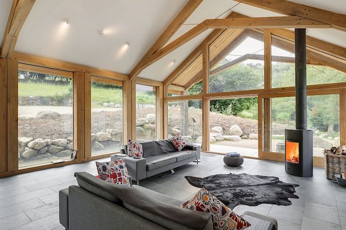 extension ossature bois et portes vitrées à encadrement de bois dans un salon à canapés gris, cheminée moderne design minimaliste