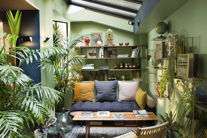 mur couelur vert, table bois et canapé gris et vert, coussin gris, blanc et jaune, multitude de vegetaux en pots par sol, deco tropicale
