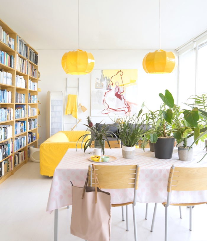 deco salon blanc aux accents jaunes et verts, pots de végétaux rangés sur une table za manger, bibliothèque bois, murs blancs