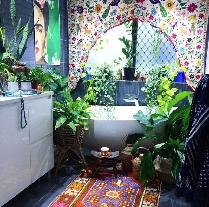 dece murale cadre frida khalo, tapis oriental sur sol carrelage gris, meuble salle de bain blanc, plusieurs végétaux autour d une baignoire, panneau textile imprimé oriental