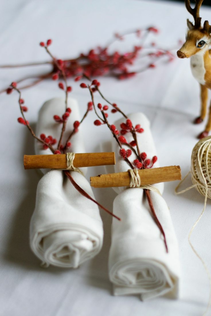 serviettes blanches attachées de manière originale, branches avec baies rouges, cerf décoratif
