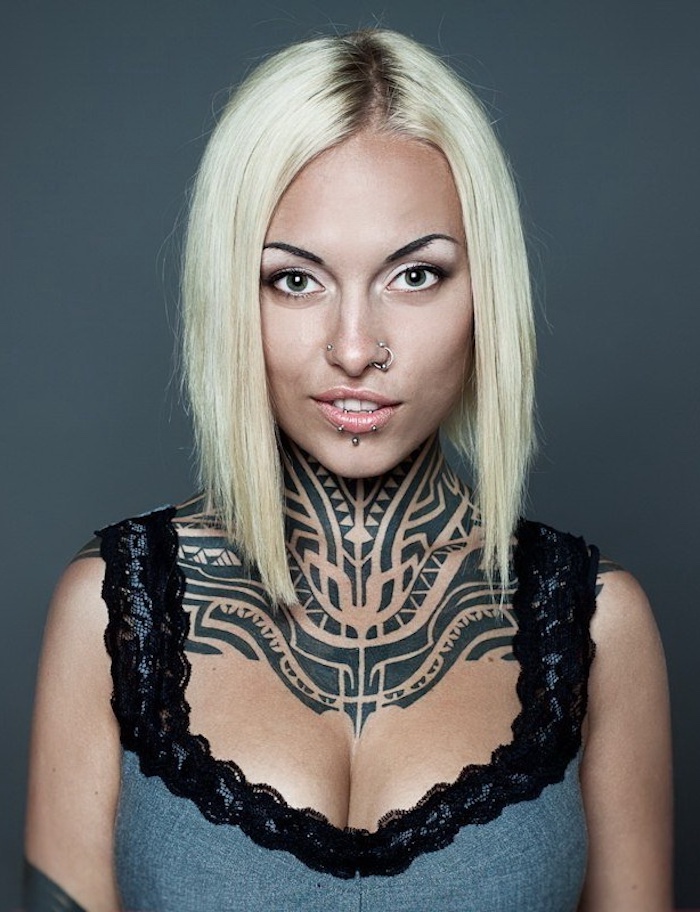 tatouage tribal cou, motifs ethniques encre noire, femme blonde, piercing nez et lèvres, débardeur dentelle