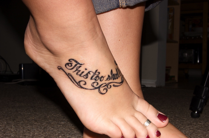 tatouage pied avec un texte en encre noire, vernis à ongles rouge, jeans, idée tatouage femme