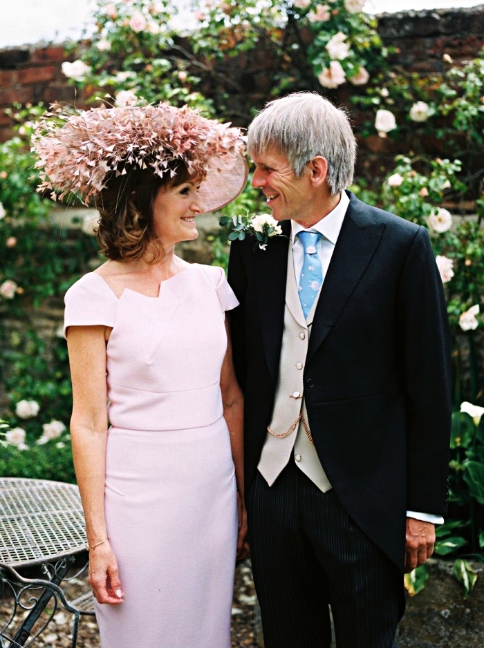 idée de tenue mariage femme 60 ans pour la mère de la mariée, robe rose à coupe droite et à manche courte avec encolure asymétrique, accompagnée d'un chapeau de mariage de la même couleur