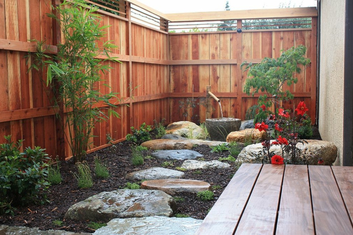 aménager un petit jardin, grandes pierres posées dans un parterre, terrasse en bois, fleurs et arbrisseaux