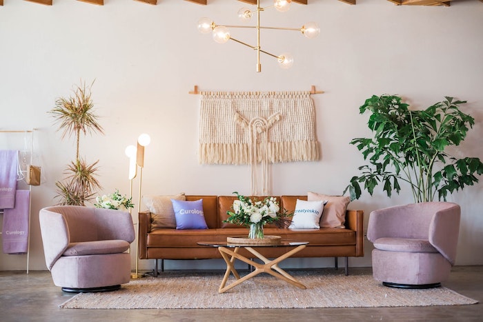 canapé en cuir marron, fauteuils rose, macramé mural pour décorer le mur, plantes vertes, palmier, quelles matériaux et matières pour aménager un salon deco nature