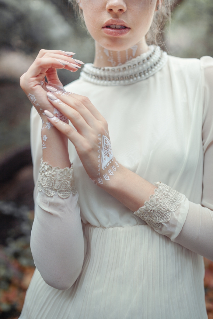 photo de henné en blanc sur la main aux motifs triangulaires, modèle robe de mariée blanche avec col perles