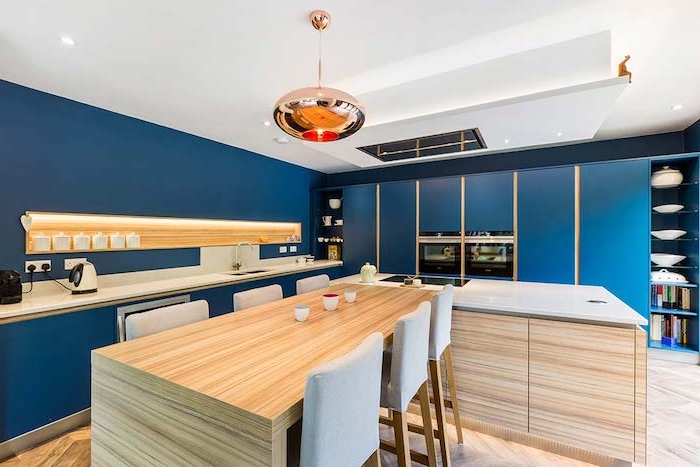 cuisine bleue outre mer avec des accents boisés introduits à travers un ilot central table bois, parquet bois clair, suspension cuivre