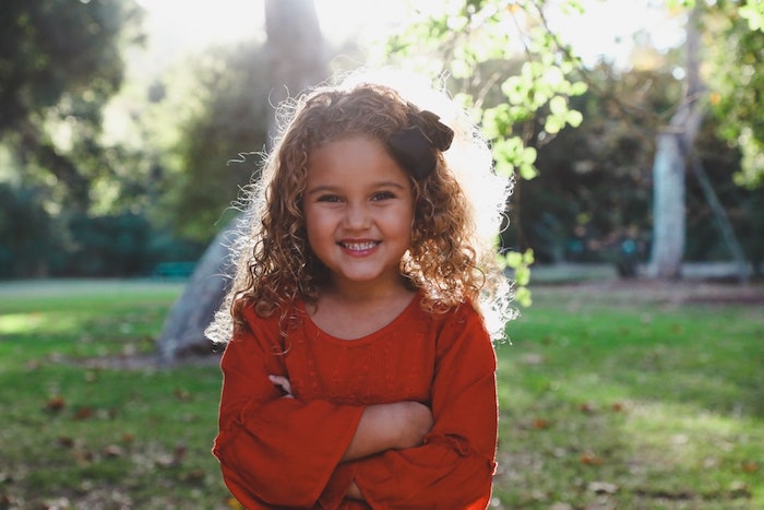 crépus-cheveux-fille-blonde-souriante-coiffure-petite-fille-coiffure-petite-fille-mariage-à-faire-soi-meme Idée comment se coiffer avec cheveux bouclés et crépus, fille blonde souriante, grande ruban sur les cheveux, coiffure pour fillette, robe rouge à manche longue évasée fille