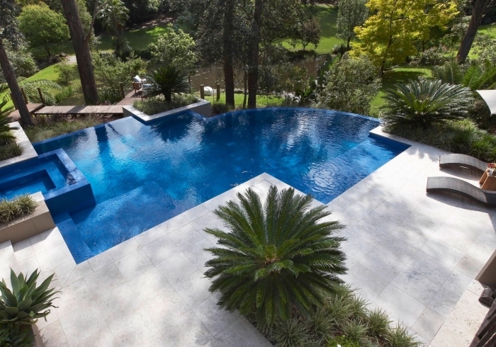 idée décoration autour d une piscine, exemple de terrasse de piscine bétonnée avec plantes vertes et transats
