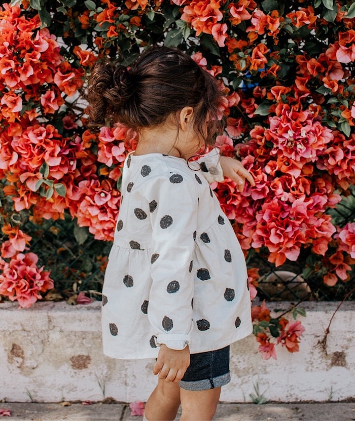 fleurs-fille-en-blouse-blanche-a-pois-noirs-queue-coiffure-petite-fille-coiffure-petite-fille-mariage-à-faire-soi-meme Adorable petite fille qui joue avec les fleurs dans la rue, coupe petite fille, coiffure facile a faire fillette cheveux