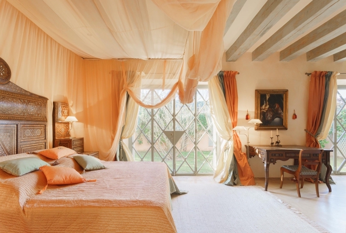 aménagement chambre spacieuse aux murs beige avec plafond à poutres bois apparentes et plancher bois clair, tete de lit design oriental