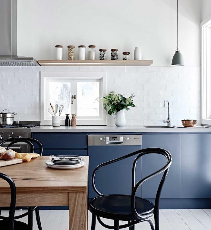 meuble bas cuisine bleu nuit avec une credence carrelage blanc étagère bois, ouverture salle à manger table bois et chaises noires en metal