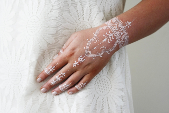 idée tatouage henné en blanc sur les mains, modèle de dessin blanc aux motifs volutes et feuilles, dessin su peau effet bracelet
