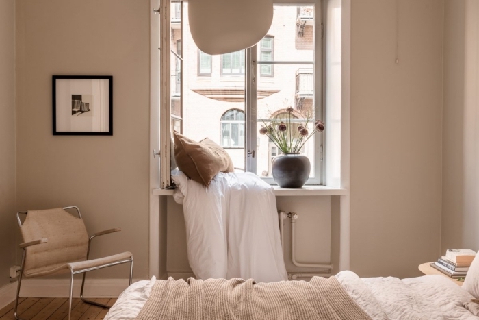 décoration petite chambre aux murs de peinture couleur sable avec fenêtre blanche, exemple de coin sous la fenêtre avec coussin marron et couverture blanche