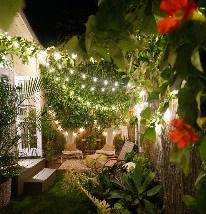 ambiance romantique dans un petit jardin avec clôture en bois, tapis beige et blanc sur sol bois extérieur décoré avec pouf