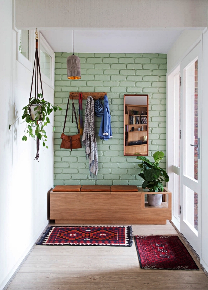 aménagement entrée de style bohème chic, banquette d'entrée en bois vintage installée contre un mur d'accent en briques peint en vert amande