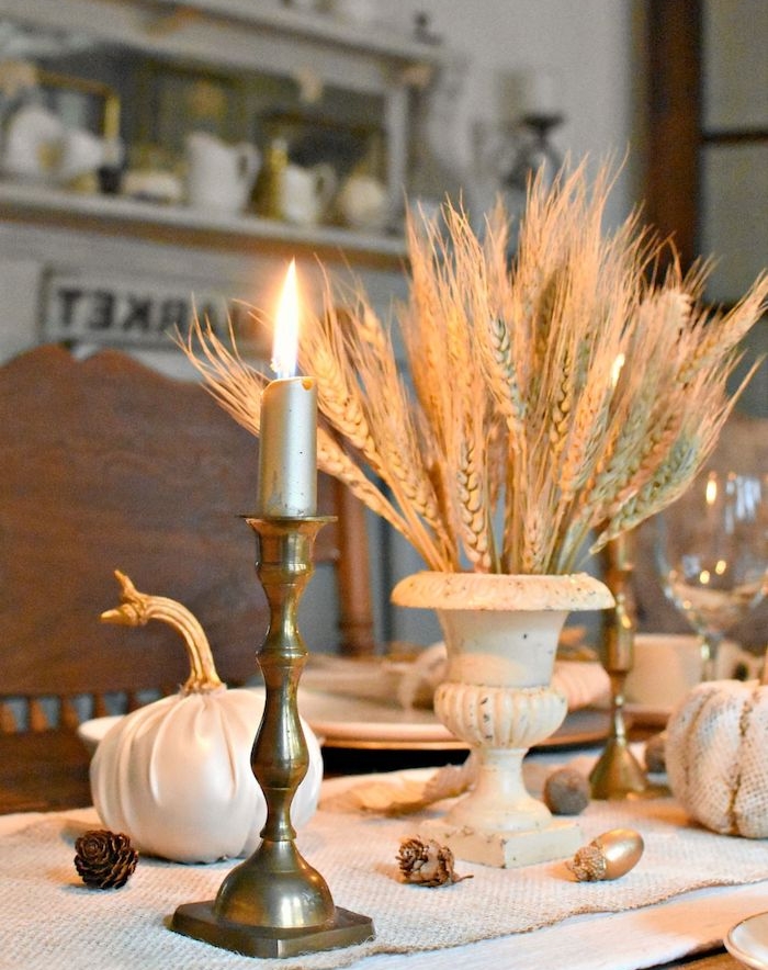 bougeoir en or et des épis de blé pour décorer un chemin de table en jute avec des pommes de pin et citrouilles habillées de tissu