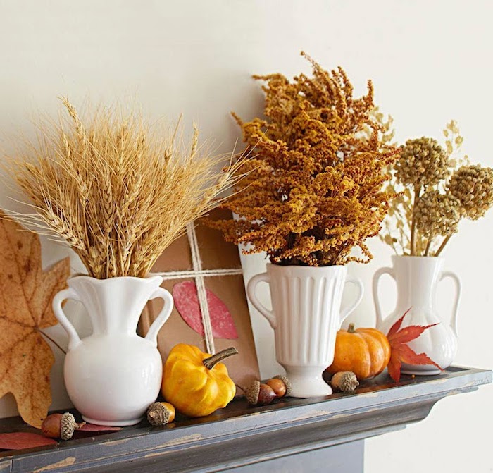 épis de blé et autres végétaux d automne dans des vases blancs de porcelaine sur le rebord d une cheminée avec deco glands, potirons et feuilles mortes