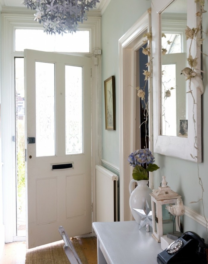 Porte d'entrée blanche, lustre décoratif, deco couloir long et étroit papier peint et peinture tendance, miroir blanc, vase avec fleurs 