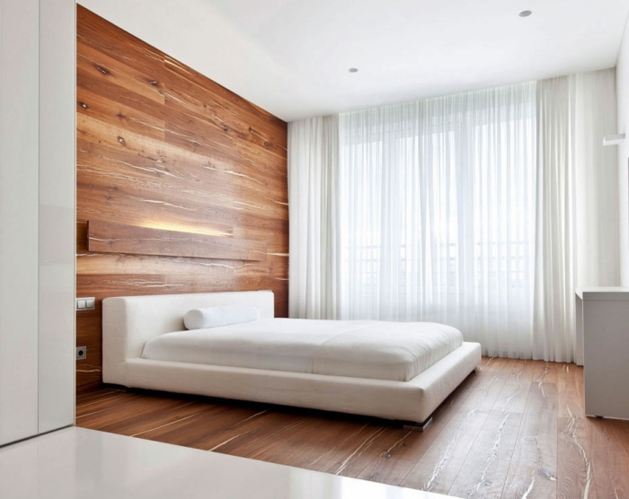 chambre adulte aménagée de style minimaliste aux murs blancs avec revêtement plancher et mur en lambris mural marron